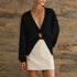 Person wearing a black open-front cardigan over a white skirt against a stone wall.