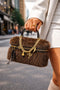 Brown fur handbag with gold chain and bow detail held by a person on a city street.
