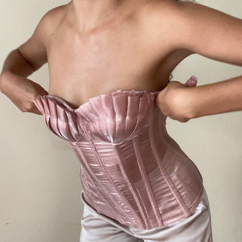 Person wearing a pink satin corset against a neutral background